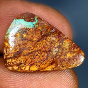 May include: A triangular, brown, green, and iridescent opal gemstone with a rough, natural finish.