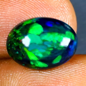 Könnte beinhalten: Ein schwarzer Opal-Edelstein mit grünen und blauen Farbschimmern. Der ovalförmige Stein ist im Cabochon-Schliff gefasst.