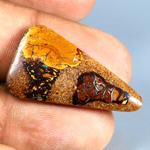 May include: A triangular, brown, orange, and red opal gemstone with iridescent flashes of colour. The opal is set in a cabochon shape and has a rough, textured surface.