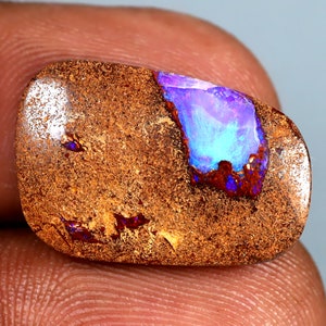 May include: A brown and orange opal gemstone with a blue and purple iridescent flash. The opal is set in a rough, natural setting.