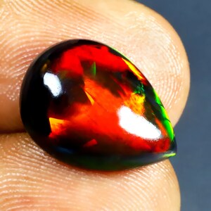 Könnte beinhalten: Ein tropfenförmiger schwarzer Opal-Edelstein mit einem feurigen, rot-orange-grünen, schillernden Farbspiel.