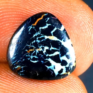 Könnte beinhalten: Ein schwarzer Opal-Cabochon mit einem weißen und orangefarbenen dendritischen Muster. Der Opal ist in einer dreieckigen Form geschnitten.