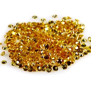 May include: A large pile of bright yellow gemstones, likely citrine or topaz, scattered on a white background.