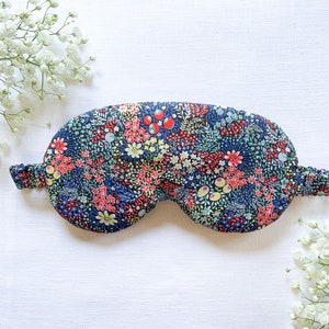 May include: A blue sleep mask with a floral pattern featuring red, yellow, and green flowers. The mask is made of soft fabric and has an elastic band to fit comfortably around the head.