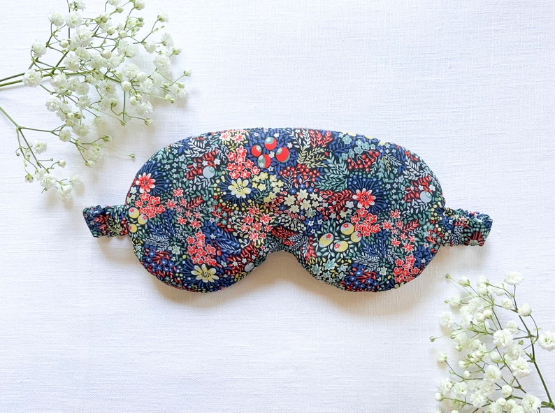 May include: A blue sleep mask with a floral pattern featuring red, yellow, and green flowers. The mask is made of soft fabric and has an elastic band to fit comfortably around the head.