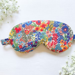 May include: A floral patterned sleep mask with a white background and colorful flowers in shades of red, blue, yellow, and green. The mask has a strap that goes around the head.