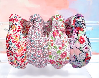 May include: Four floral patterned headbands in pink, red, and blue. The headbands are made of fabric and have a knotted design.