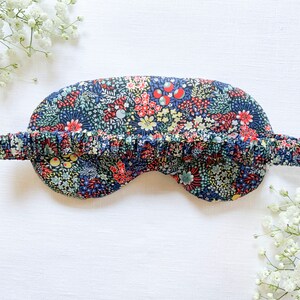May include: A blue sleep mask with a floral print featuring red, yellow, and green flowers. The mask has a ruffled elastic band.