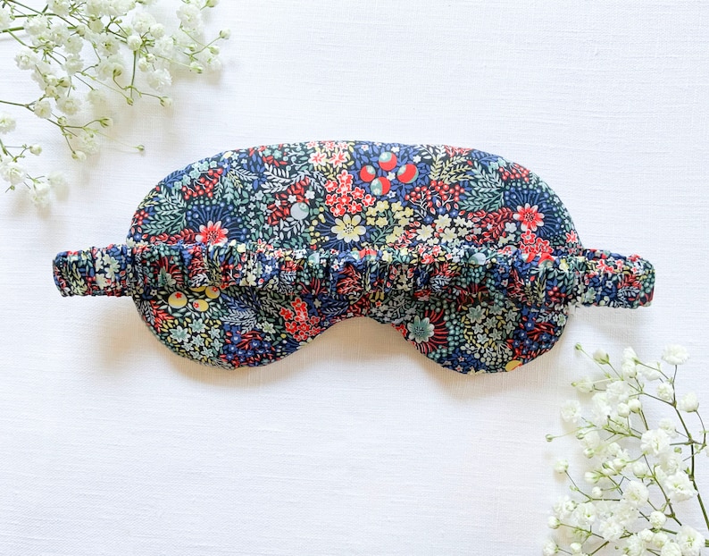 May include: A blue sleep mask with a floral print featuring red, yellow, and green flowers. The mask has a ruffled elastic band.