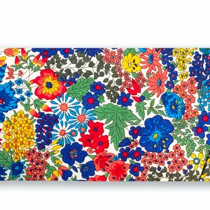 May include: A white fabric clutch with a floral print featuring red, blue, yellow, and green flowers. The clutch has a flap closure and a white background.