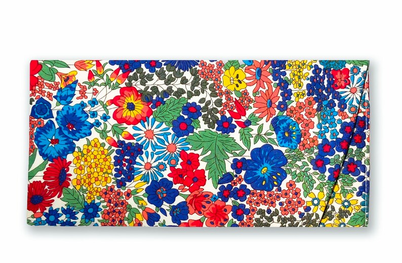 May include: A white fabric clutch with a floral print featuring red, blue, yellow, and green flowers. The clutch has a flap closure and a white background.