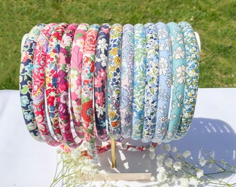 May include: A collection of colorful floral patterned headbands in various shades of blue, pink, and red. The headbands are arranged in a circle on a white surface.