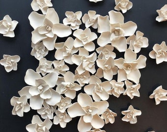 May include: A wall art piece featuring a cluster of white ceramic flowers on a black background. The flowers are arranged in a random pattern, creating a textured and organic look.