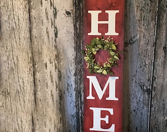 May include: Red wooden sign with the word "HOME" in white letters. The "O" is decorated with a green wreath. The sign also says "Welcome to our" and "Sweet Home".