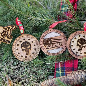 May include: Four wooden Christmas decorations featuring the phrase "Let's Go Brandon" and the acronym "FJB" on each. The decorations are adorned with stars, an American flag, and a skull.