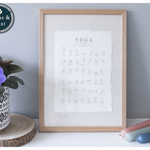 以下が含まれることがあります： 「YOGA」という言葉と、ミニマルなスタイルのヨガポーズのリストが書かれた額装されたプリント。プリントは白い背景で、明るい木製のフレームに入っています。