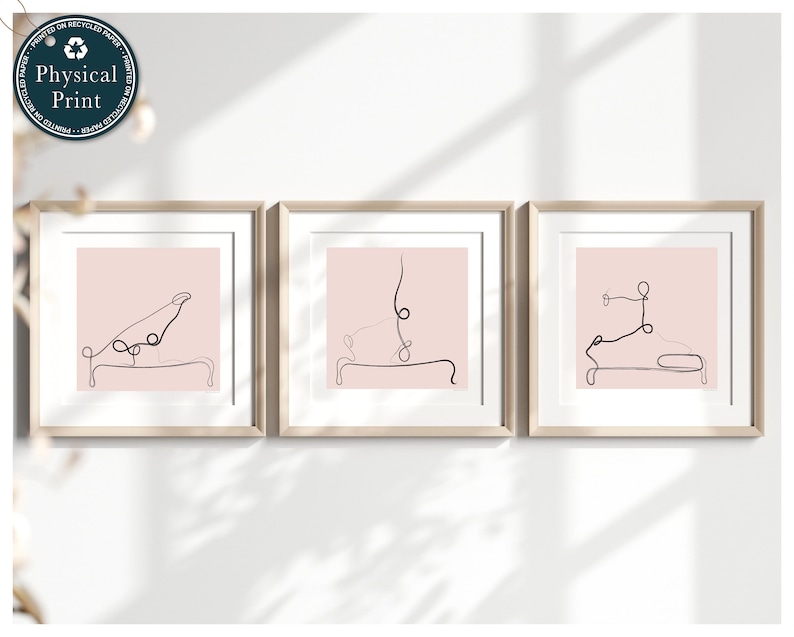 Op de afbeelding: Drie ingelijste prints met een roze achtergrond en zwarte lijntekeningen van mensen die yogaposes doen op een reformer.