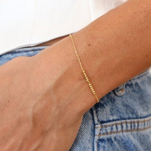 May include: A gold chain bracelet with a row of small gold beads.