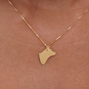 May include: A gold-colored necklace featuring a pendant shaped like a dog's head. The pendant hangs from a delicate chain. The necklace is worn against a white top.