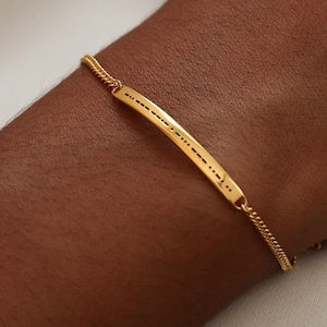 May include: A gold chain bracelet with a thin, rectangular bar charm. The bar has a delicate pattern of dots.