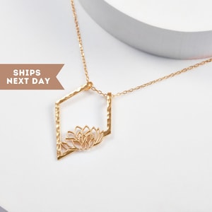 May include: Gold-colored necklace with a geometric pendant featuring a lotus flower design. The pendant is a hammered hexagon shape. The chain is delicate and the necklace is on a white background.