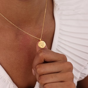 May include: A gold-colored necklace with a delicate chain and a round pendant. The pendant is inscribed with the words "love you most" and a small heart symbol. The necklace is being held up by a person.
