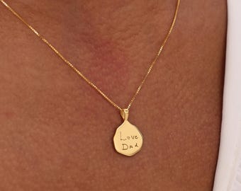 May include: A gold-colored pendant necklace with a delicate chain. The pendant is a rounded shape with the handwritten text "Love Dad" engraved on it. The necklace is worn around the neck.