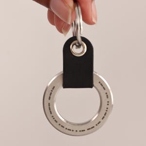 May include: A silver keyring with a black leather loop and a circular metal tag with a pattern of dots around the edge.