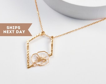Può includere: Una collana color oro con un ciondolo geometrico dalla texture martellata. Il ciondolo incornicia un delicato motivo floreale. La collana è su sfondo bianco. Il testo a sinistra dice "SHIPS NEXT DAY".