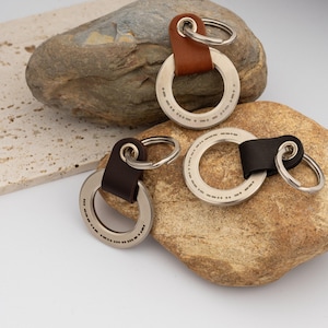 May include: Three keychains with a circular design and a leather strap. The keychains have a silver ring with dotted markings and a small metal ring attached to the leather. One keychain has a brown leather strap, and two have a dark brown leather strap.