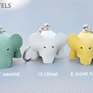 May include: Three leather elephant keychains in pastel colors: mint green, white, and yellow. Each keychain has a silver-colored ring and a small loop for attaching keys. The text "LES PASTELS" is at the top.