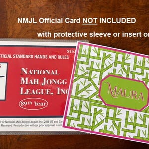 May include: A protective sleeve containing a red National Mah Jongg League 2026 official standard hands and rules card, alongside a white insert featuring a green bamboo pattern and a central pink-bordered hexagon with the name Maura printed.