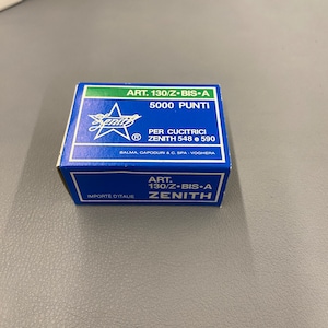 Peut inclure: Une boîte bleue et verte avec le texte "ART. 130/Z-BIS-A 5000 PUNTI" et "PER CUCITRICI ZENITH 548 e 590" sur le devant. La boîte a également un logo en forme d'étoile avec le mot "ZENITH" à l'intérieur.