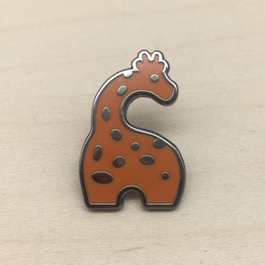 May include: A whimsical orange giraffe enamel pin with dark brown spots and a silver-colored outline. The giraffe pin is a cute accessory for jackets, bags, or hats. The pin is a fun, animal-themed accessory.