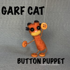 May include: A needle-felted orange cat puppet with black ear tufts, black bead eyes, and a yellow muzzle. The puppet features orange button hands and feet, suspended by thin white strings. The text GARF CAT BUTTON PUPPET is visible.