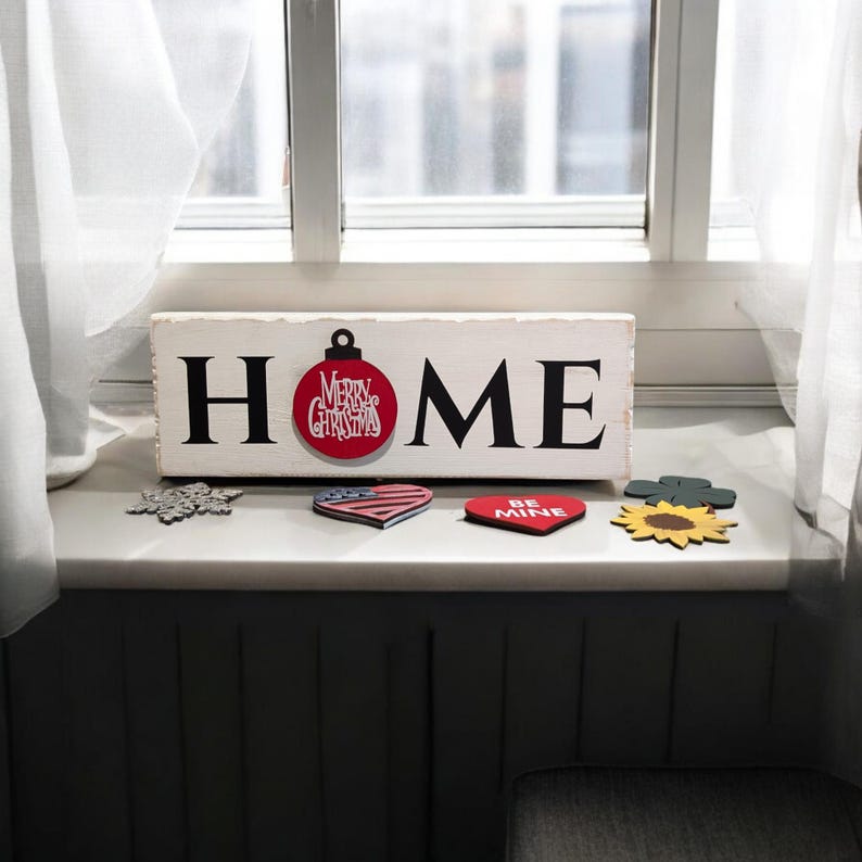 May include: A white wooden sign with the word "HOME" in black letters. A red ornament with "Merry Christmas" text is attached to the "O". Decorative wooden shapes, including a snowflake, heart, and sunflower, are arranged below.