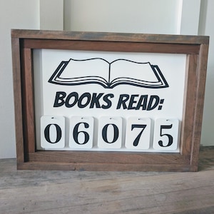 May include: A wooden framed sign with the words "BOOKS READ:" and an illustration of an open book. Below the text are four white number tiles displaying "06075". The frame is a dark brown color.