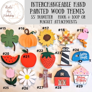May include: A collection of interchangeable, hand-painted wooden themes, each approximately 3.5 inches in diameter. Designs include a four-leaf clover, pumpkin, sunflower, maple leaf, flamingo, watermelon, apple, strawberry, lighthouse, and camper.