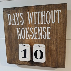 May include: A wooden sign with the text "DAYS WITHOUT NONSENSE" and a white flip counter with the number "10" displayed.