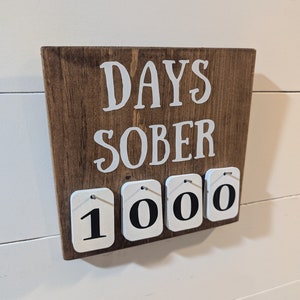 May include: A wooden sign with the text "DAYS SOBER" and a set of white number tiles displaying "1000".