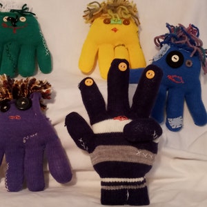May include: Five colorful finger puppets made from repurposed gloves. Each puppet has a unique face and hair made from yarn. The puppets are green, yellow, blue, purple, and blue and white striped.