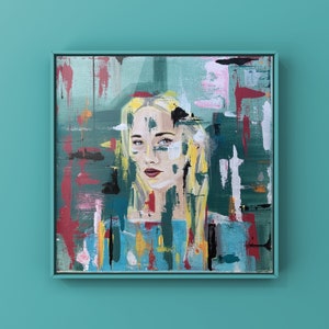 May include: Square framed abstract portrait painting. The artwork features a woman with blonde hair and a blue top. The background has brushstrokes of green, red, white, and yellow. The frame is a matching teal color.