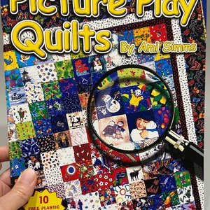 May include: A book titled "Picture Play Quilts" by Ami Simms. The cover features a colorful patchwork quilt with a magnifying glass highlighting a section of the quilt. The book includes 10 free plastic templates.
