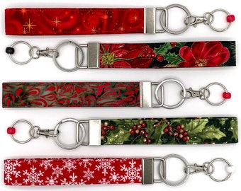 May include: Five different keychains with red and green fabric and silver key rings. Each keychain has a different Christmas-themed pattern.