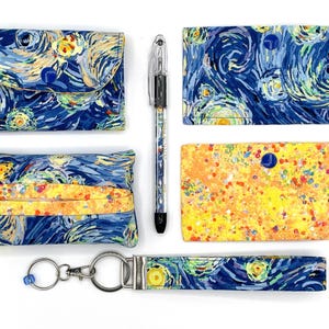 May include: A collection of fabric accessories featuring a starry night design. Includes a small wallet, a card holder, a tissue holder, a key fob, and a pen. The items are primarily blue with yellow and white accents.