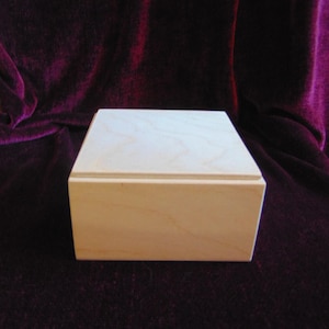 May include: A plain wooden box with a lid. The box is made of light wood and has a smooth finish.