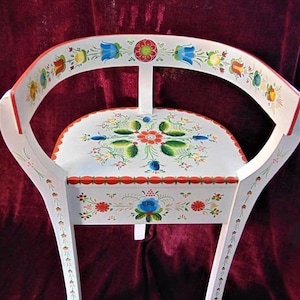 May include: A white wooden chair with a curved back and hand-painted floral designs in red, blue, green, and yellow. The chair is decorated with a traditional folk art style.
