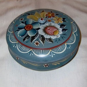 May include: A round wooden box with a blue painted lid. The lid is decorated with hand-painted flowers in shades of blue, red, yellow, and white. The box is a traditional folk art piece.