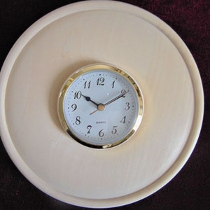 May include: A round, wooden clock with a white face and gold trim. The clock has black hands and black numbers. The clock is set to 10:10.