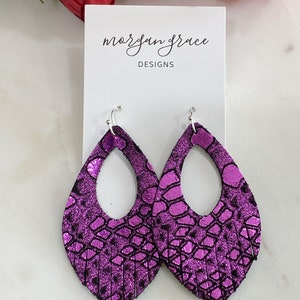 Op de afbeelding: Paarse leren oorbellen met een franje detail en een uitgesneden ovale vorm. De oorbellen zijn op een witte kaart met de tekst "morgan grace DESIGNS".